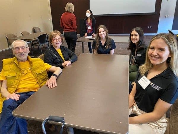 A group of people sitting around a table smiles for the camera.