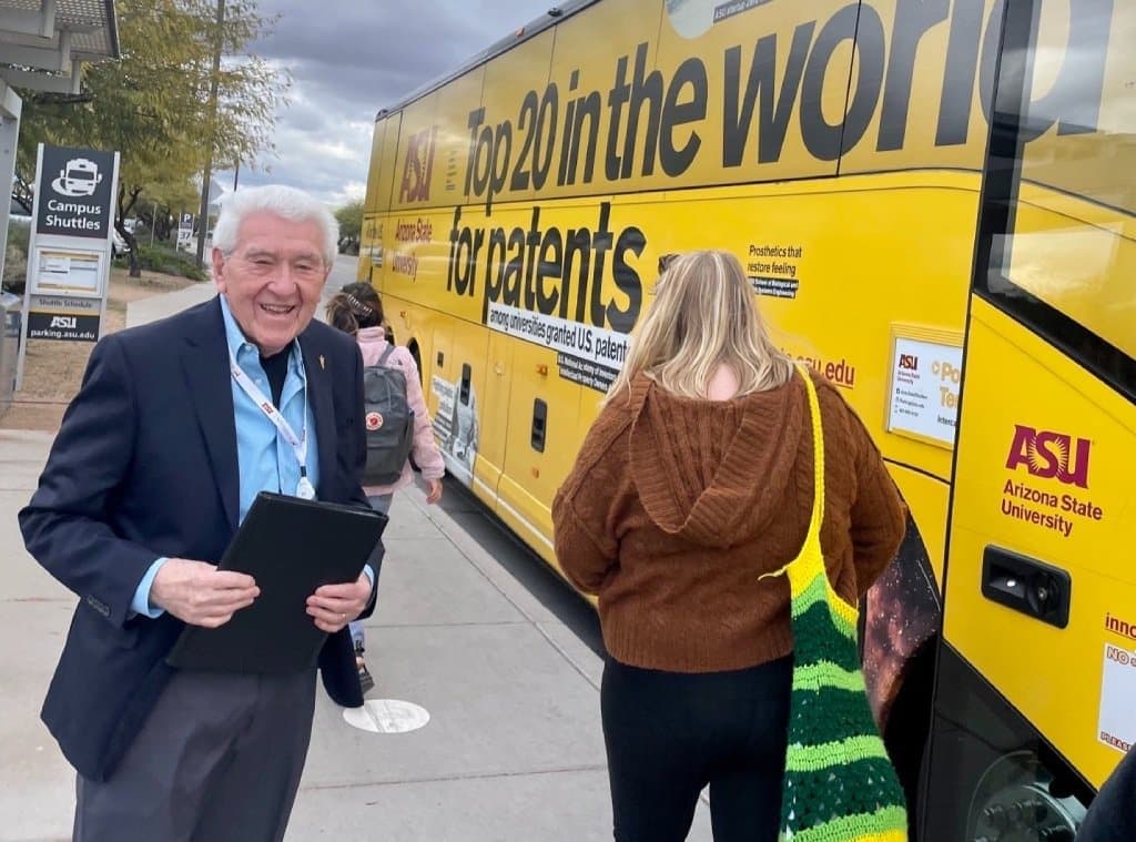 Candid shot of an older man holding a laptop or tablet standing by a bus.